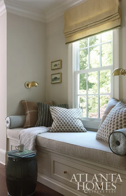 Window seat with neutral cushions and patterned pillows, flanked by brass sconces.