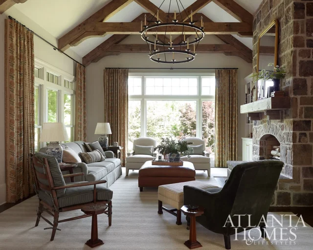 Living room with exposed beams, stone fireplace, and patterned curtains.