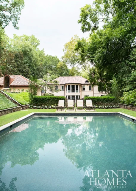 Tuscan-style home with red tile roof, surrounded by lush greenery, overlooking a swimming pool with