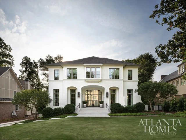 White brick house with arched entryway and large windows. Atlanta Homes & Lifestyles logo.