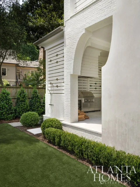 White brick outdoor kitchen with stainless steel grill and arched entryway.