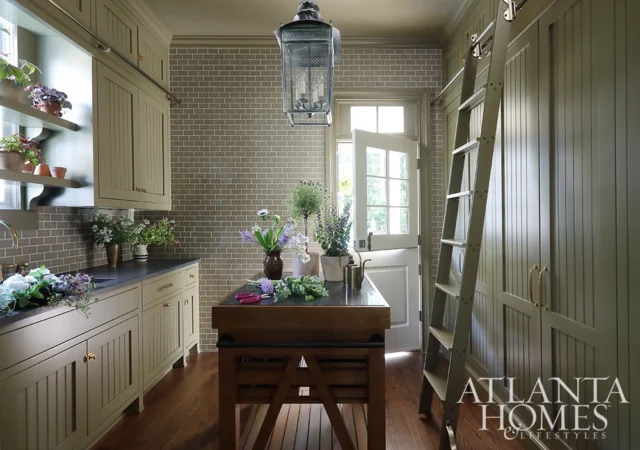 Kitchen with taupe subway tile backsplash, sage green cabinetry, butcher block island, and ladder.