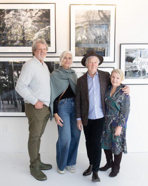 Four people standing in front of framed photographs on a white wall.