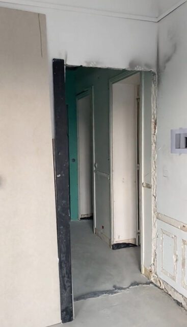 Hallway with unfinished walls, doorways, and doors. Light gray floor.
