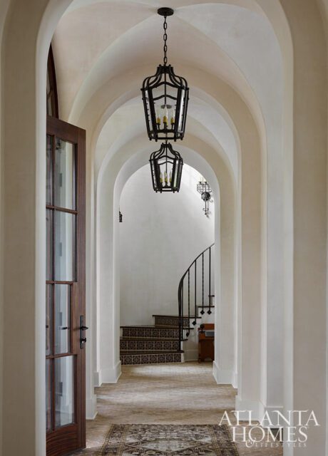 Hallway with arched ceilings, dark metal lanterns, and a curved staircase with patterned tile
