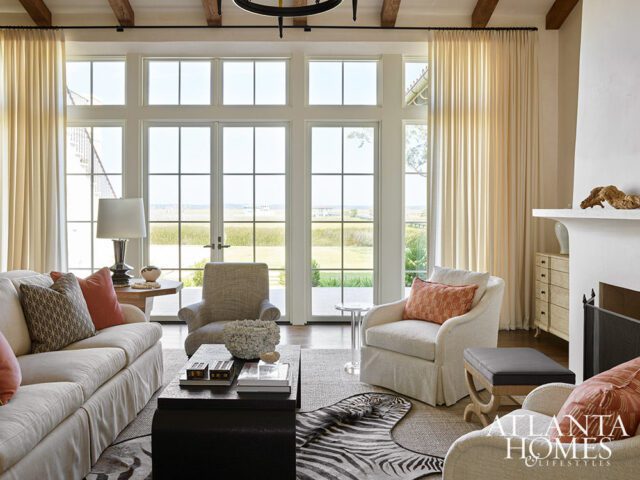 Living room with cream sofa, chairs, dark coffee table, and large windows overlooking a marsh.