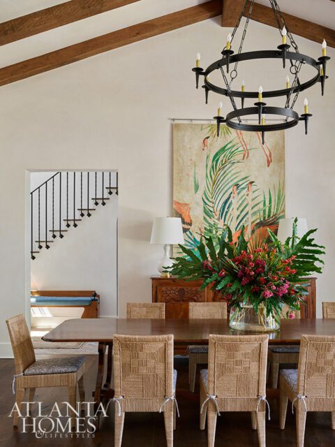 Dining room with wood table, woven chairs, tropical art, and chandelier