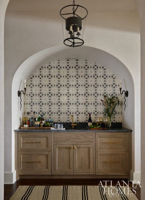 Bar area with patterned tile backsplash, wood cabinetry, stone countertop, and brass faucet.