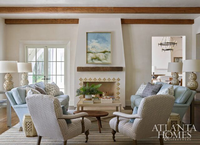 Living room with light blue sofas, patterned armchairs, fireplace with artwork, and wood beams