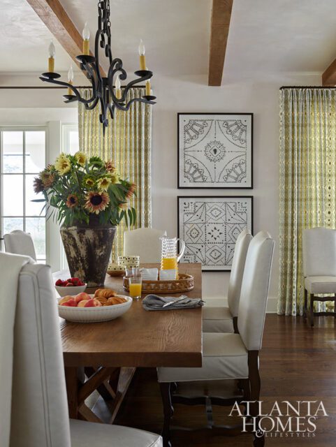 Dining room with wooden table, white chairs, floral arrangement, and framed art.