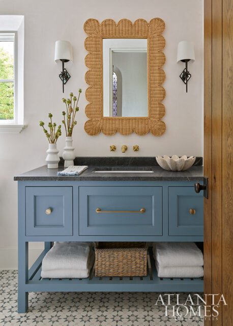 Blue vanity with wicker mirror, stone countertop, and brass fixtures.