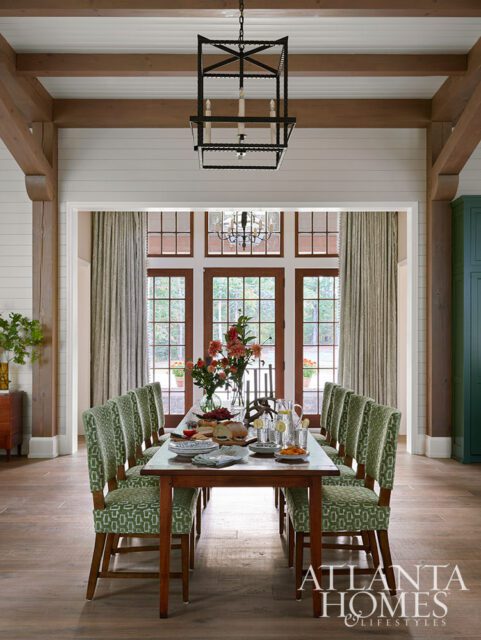Dining room with wooden beams, green patterned chairs, and a table set for a meal.