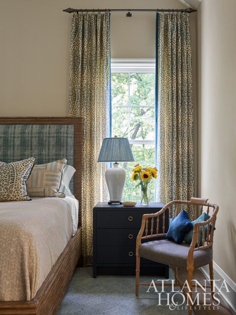 Bedroom with wood bed, patterned curtains, dark blue nightstand, and bamboo chair.