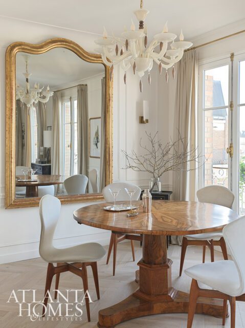 Dining room with round wood table, upholstered chairs, and large gold mirror