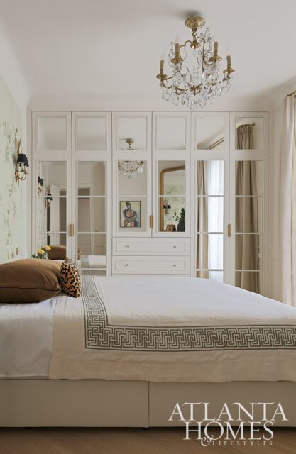 Bedroom with mirrored closet doors, crystal chandelier, and Greek key trim on bedding.