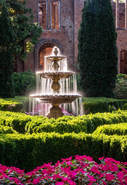Tiered fountain in a formal garden with manicured hedges and pink flowers