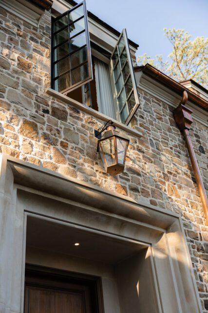 Stone house exterior with open casement windows and copper downspout