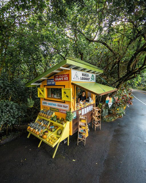Yellow fruit stand with pineapples, avocados, and bananas. Signage for shave ice and smoothies.