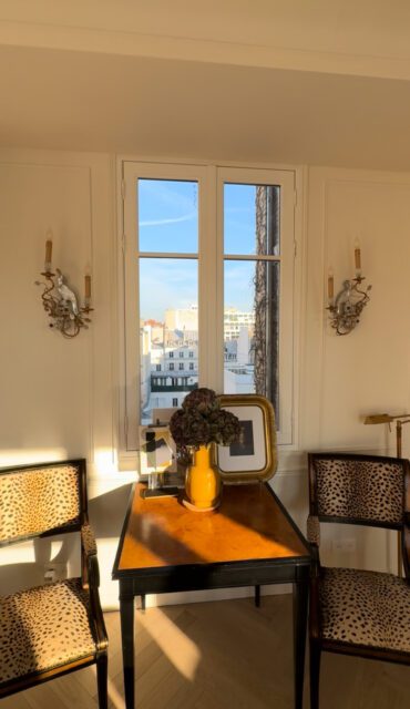 Two chairs with leopard print upholstery flank a table with a yellow vase and framed art.