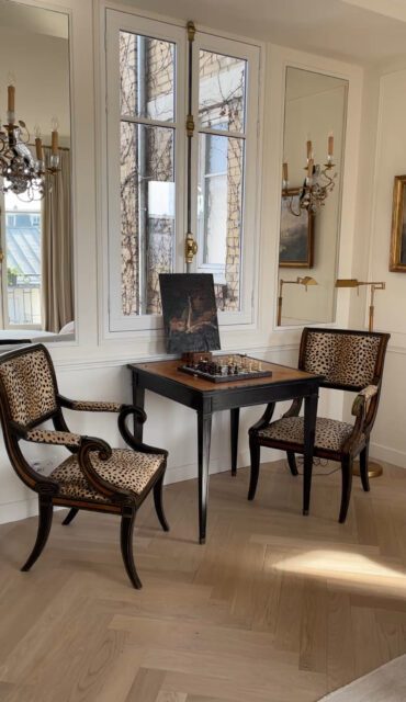 Room with two chairs upholstered in leopard print fabric, a table with a chessboard, and a painting.