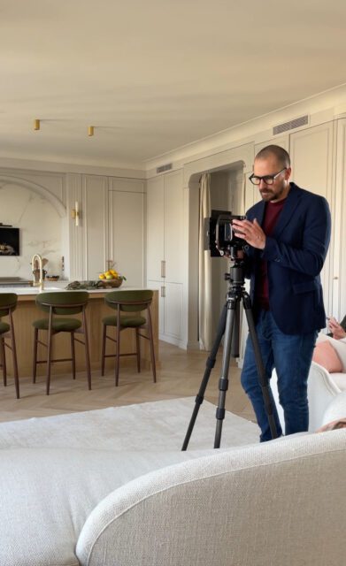 Man with camera on tripod in modern kitchen with island and green stools