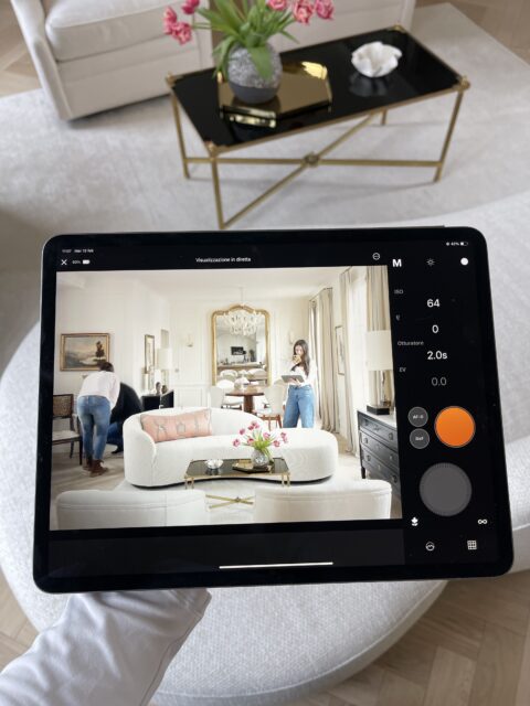 Tablet displaying a living room with two people, a white sofa, and a black coffee table. Camera