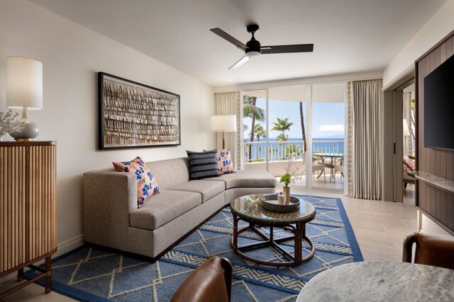 Living room with sectional sofa, blue geometric rug, rattan coffee table, and ocean view balcony.