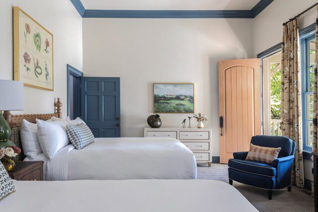 Bedroom with two queen beds, blue door, peach door, and blue armchair.