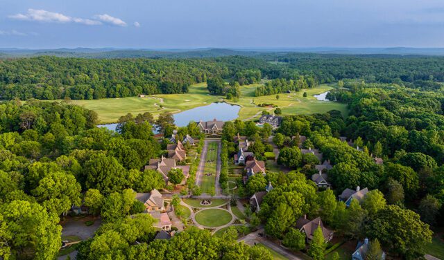 Aerial view of a village with houses, a lake, and a golf course surrounded by trees.