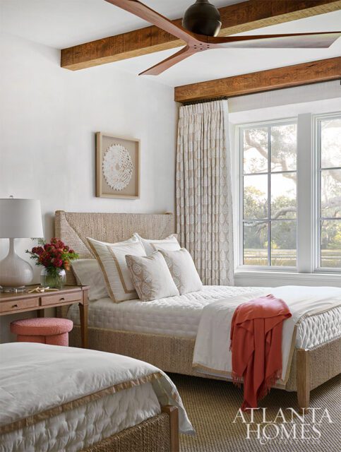 Bedroom with two beds, white bedding, woven headboards, wood beams, and large windows.