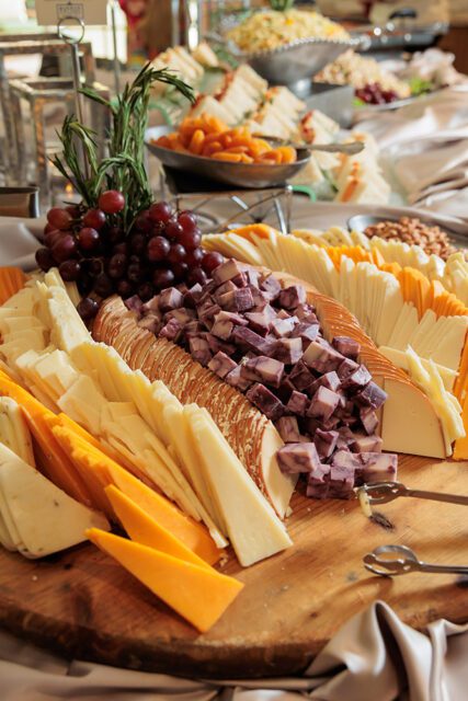 Wooden board with sliced cheeses, grapes, rosemary, and crackers