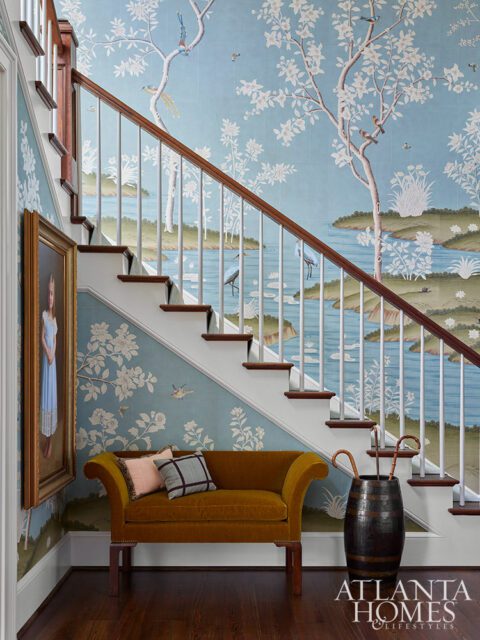 Staircase with chinoiserie wallpaper, mustard velvet settee, and barrel umbrella stand.
