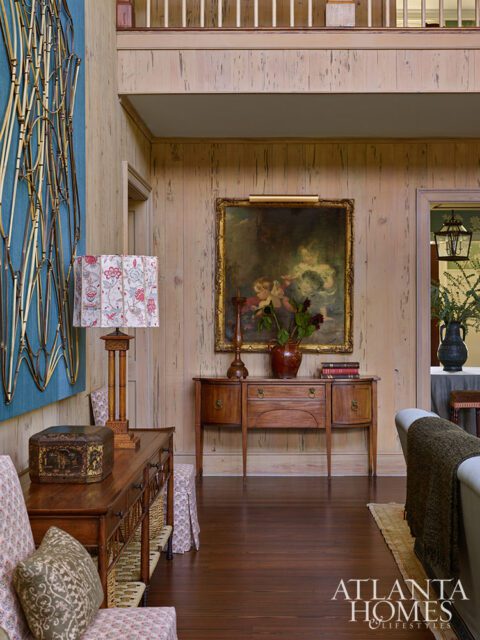 Wood paneled room with antique furniture, artwork, and a lamp.