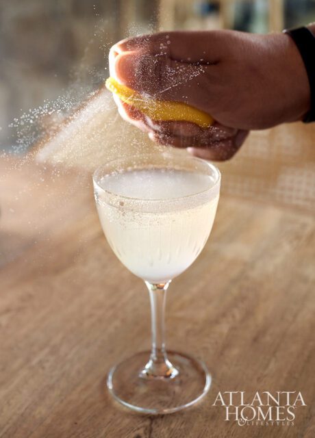 Hand squeezing lemon peel over a cocktail glass with a sugar rim.