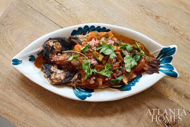 Whole grilled fish in a fish-shaped platter with sauce and cilantro.