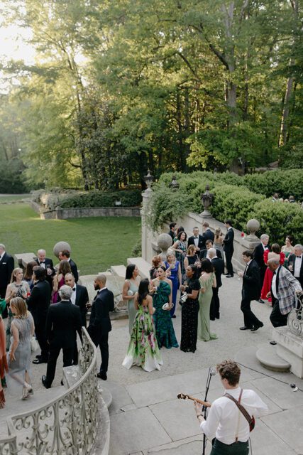 People in formal attire gathered on stone steps with a musician playing guitar.