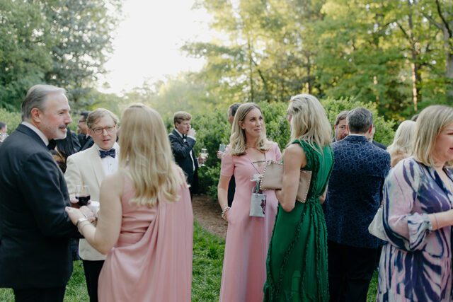 People in formal attire mingling outdoors at a garden party