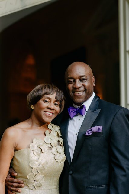 Couple smiling, woman in gold dress, man in tuxedo with purple bow tie