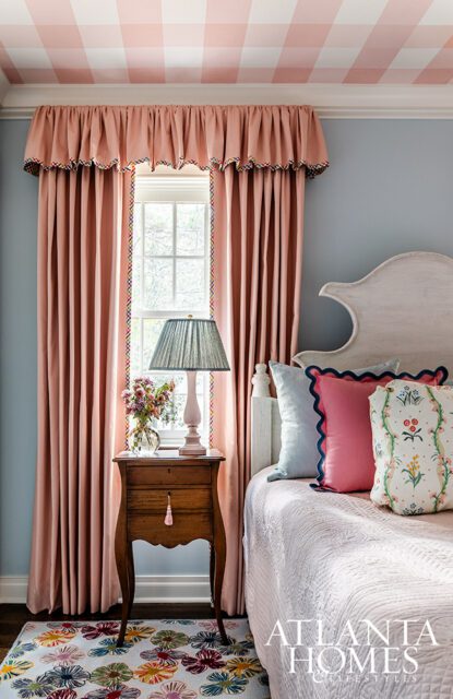 Bedroom with pink gingham ceiling, pink curtains, and a bed with colorful pillows.