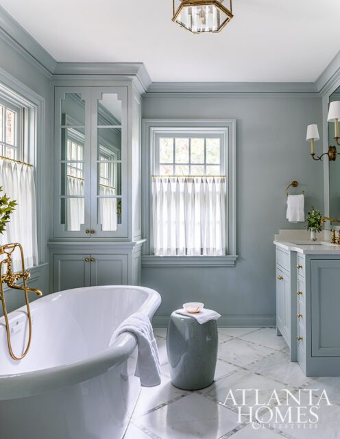 Pale blue bathroom with freestanding tub, marble floor, and custom cabinetry.