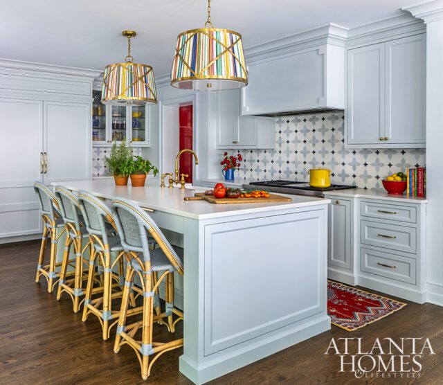 Light blue kitchen with island, bar stools, patterned backsplash, and colorful pendant lights.