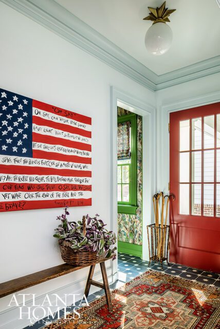 Entryway with American flag art, red door, patterned rug, and basket of plants.