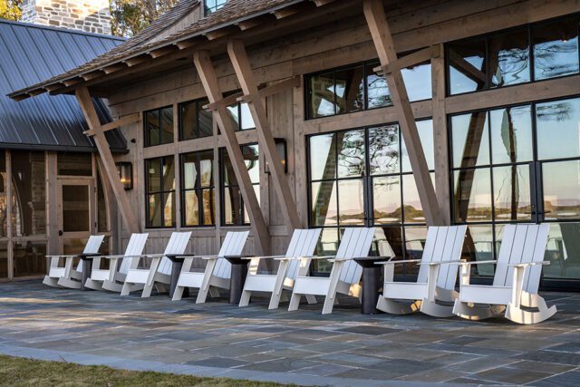 Wooden lodge with large windows and white Adirondack chairs on stone patio