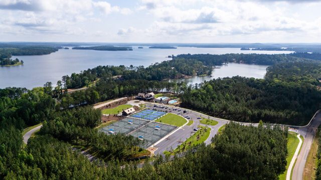 Aerial view of tennis courts and a clubhouse on a lake surrounded by trees