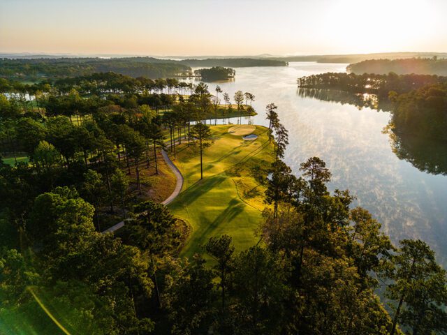 Golf course with a lake at sunrise, surrounded by trees.