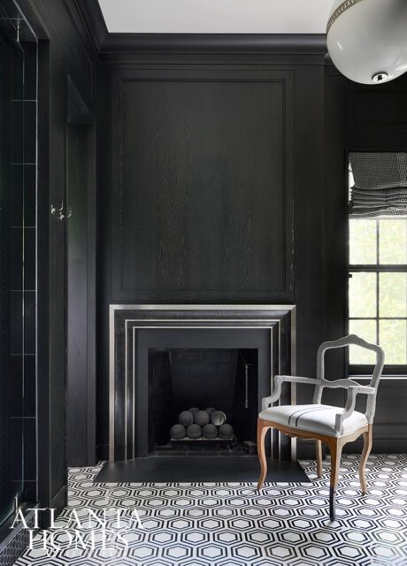 Black paneled room with fireplace, hexagonal tile floor, and upholstered chair.
