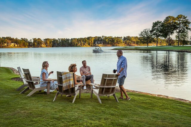 Four people relaxing by a lake with a boat in the distance.