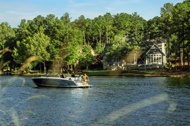 Boat with two people on a lake with houses and trees in the background.