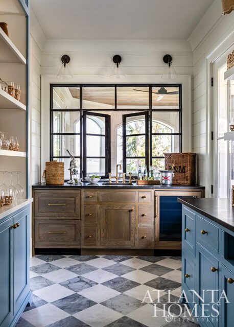 Bar area with wood cabinetry, black countertop, and large black-framed windows overlooking a lake.