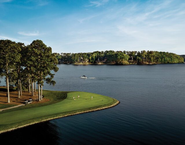 Golf course on a lake with trees and houses on the far shore.